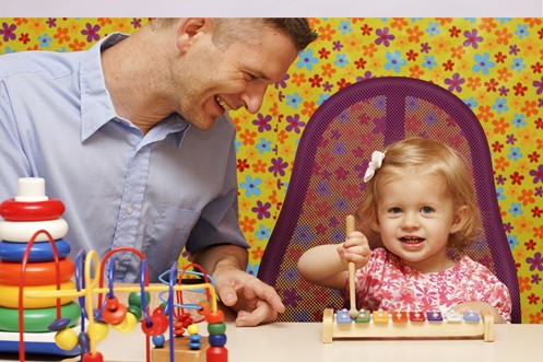 Foto: Ergotherapeut spielt mit kleinem Mädchen vor bunter Tapete, Bildnachweis: Köpenicker auf Adobe Stock, https://stock.adobe.com/de/images/ergotherapie-padiatrie/41268347