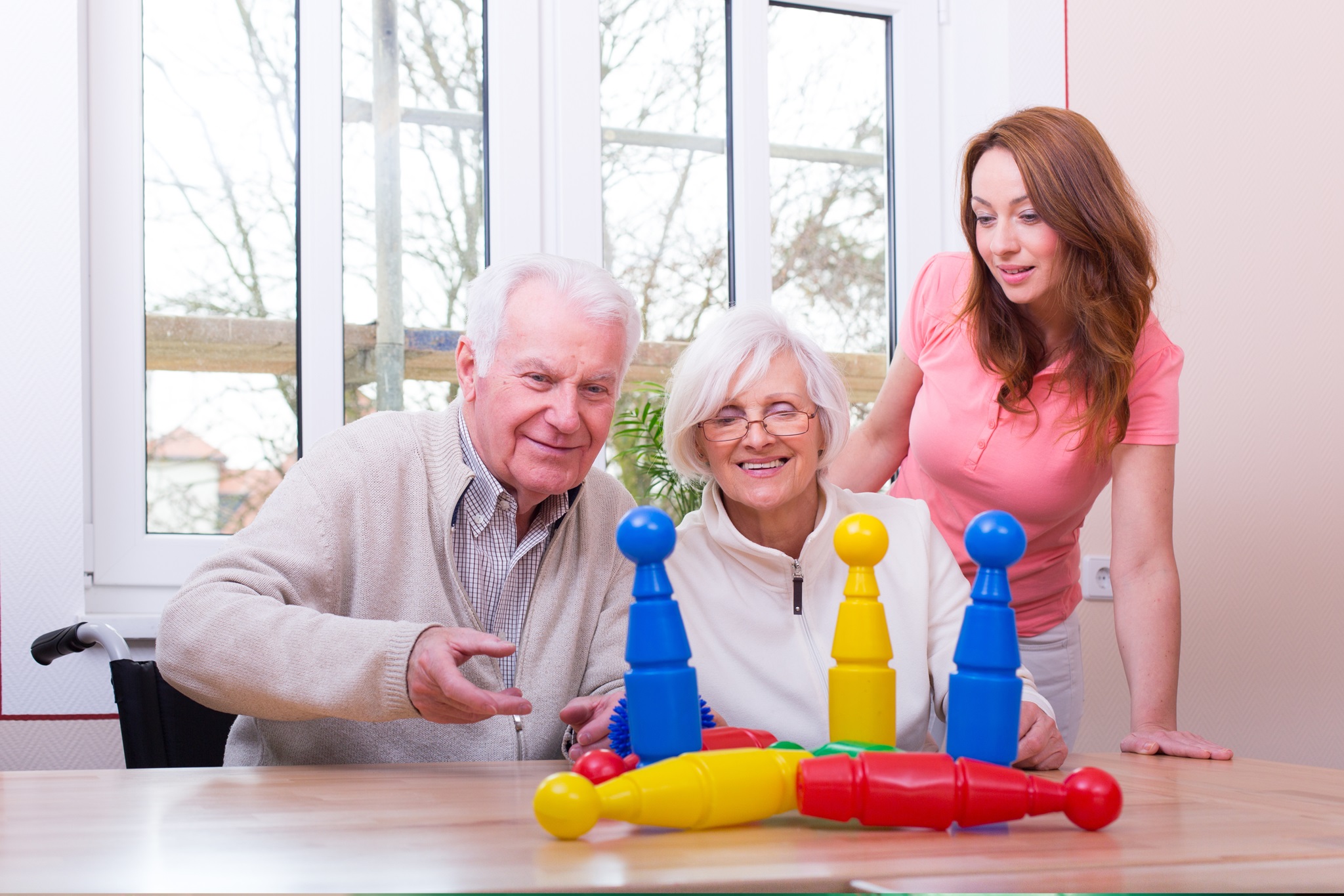 Foto: Senioren spielen mit bunten Kegeln, Ergotherapeutin steht zuschauend daneben, Bildnachweis: drubig-photo auf Adobe Stock, https://stock.adobe.com/de/images/gluckliches-seniorenpaar-spielt-kegeln/63351680